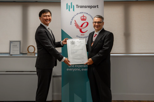 Photo of Jay Shen and Mr Kevin McGrath OBE MRICS DL smiling, holding the official King’s Award certificate together. They stand in front of the Transreport King’s Award for Enterprise in Innovation banner.