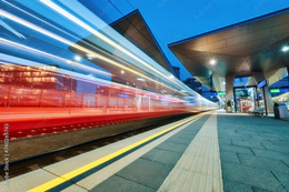 Photo of a red train speeding past a platform with a blur effect to convey movement.
