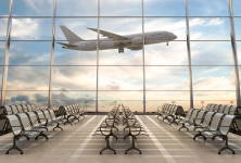 Empty airport seating area with a large window showing an airplane taking off against a cloudy sky.