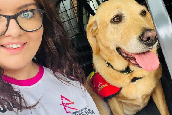 Emma Partlow, a white female and Transreport's Accessibility & Inclusion Manager, sitting beside her assistance dog Luna.