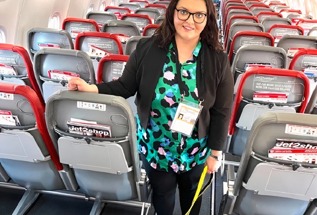 Emma Partlow, Transreport's Inclusion & Accessibility Manager, standing beside her assistance dog Luna, in the middle aisle of a commercial passenger aeroplane.