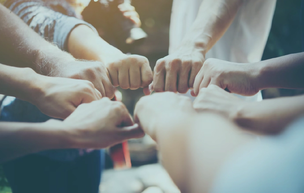 A close-up of many clenched fists touching in a circle.