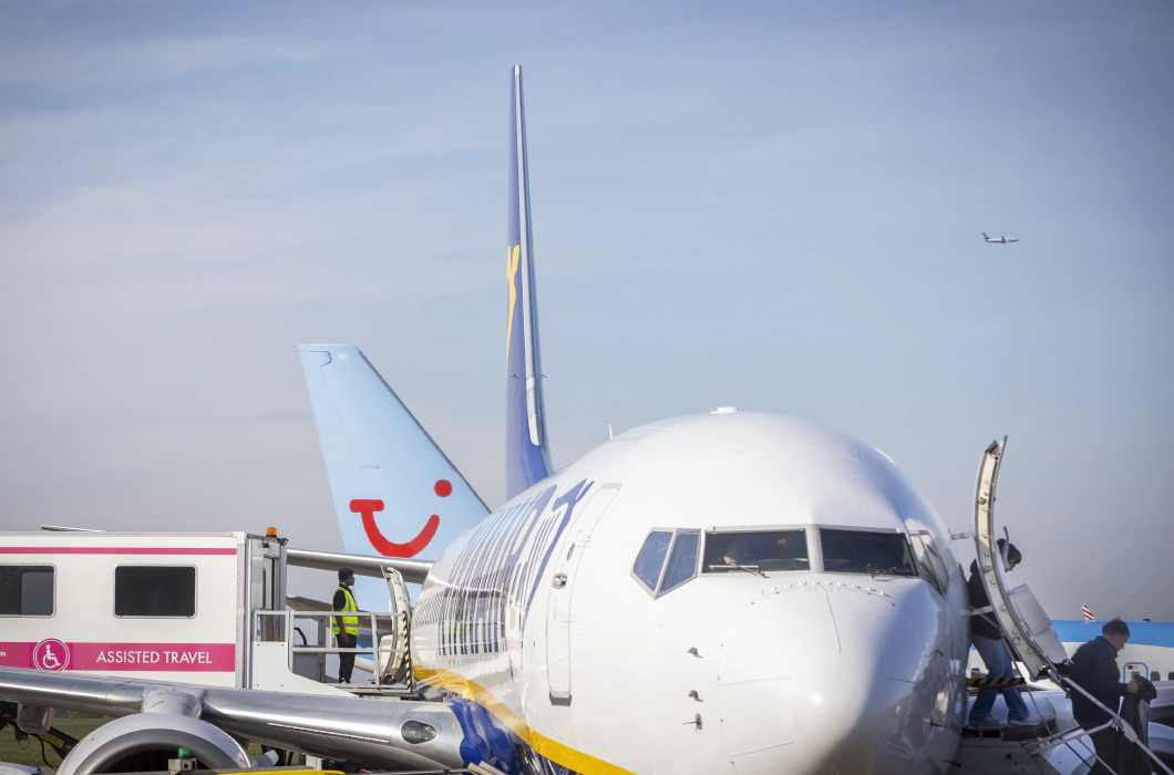 航空業界におけるアクセシブルな旅の変革:Transreportがイースト・ミッドランズ空港と提携 A zoomed in photograph of a Ryanair Boeing 747 plane from the front, with passengers disembarking by the front exit, by stairs, on the right, and an ambulift docking with the central exit of the plane on the left.