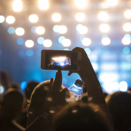 A photo of fans at a concert A photo of fans at a concert with one person taking a photo of the illuminated stage on their smart phone.