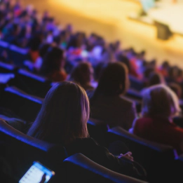 A photo of theatre-style seats in a venue packed with people. A photo of theatre-style seats in a venue packed with people.