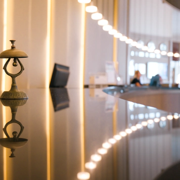 Hotel Photo of a hotel check-in desk with a bell in the foreground and a customer speaking to a member of staff in the background.
