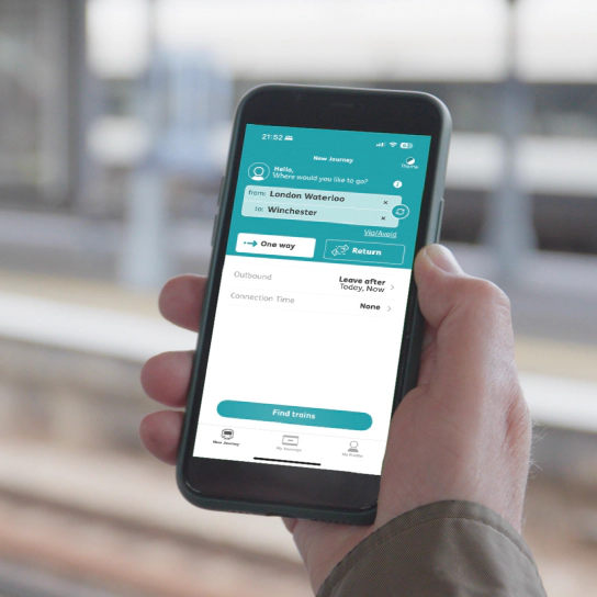 New Journey page in the PA App A photo of a person’s hand holding a smart phone showing the New Journey page in the PA App beside a train platform.