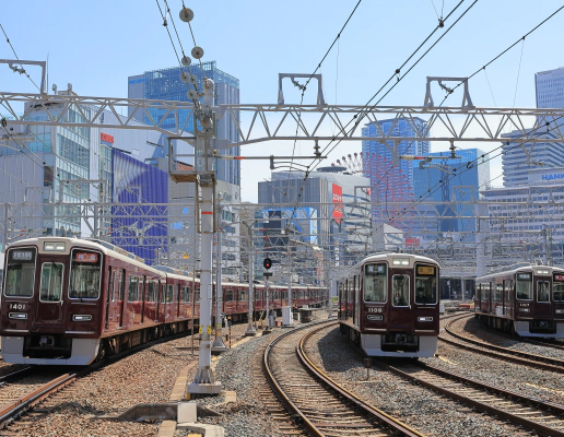 Two red trains moving along train tracks at a Japanese train station.