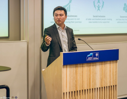 Jay Shen, an asian man with short black hair, and CEO of Transreport, in a grey suit standing at a speaking podium. Jay Shen, an asian man with short black hair, and CEO of Transreport, in a grey suit standing at a speaking podium.