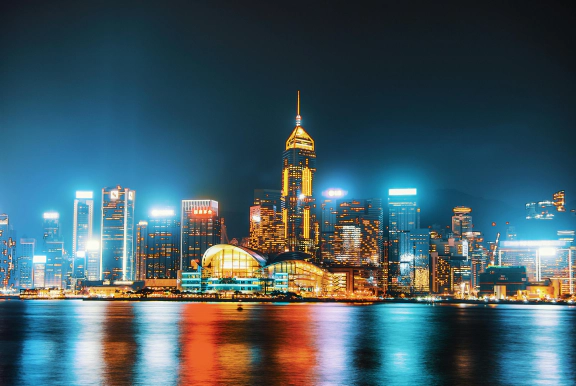 A photo of a glowing city skyline with illuminated skyscrapers at night, reflecting in a river.
