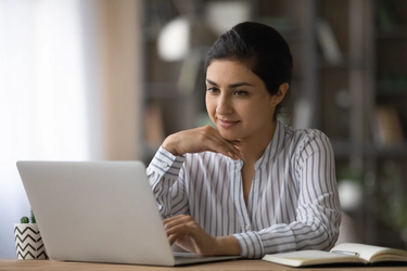 A woman in a blouse sitting in front of an open laptop computer.