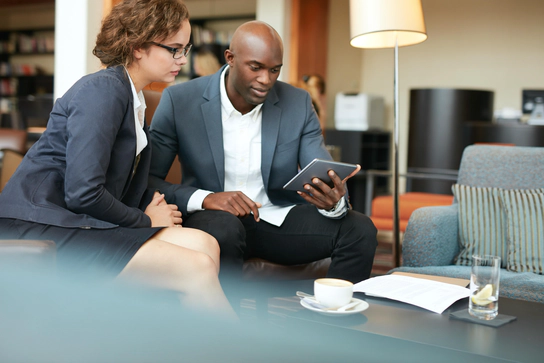 Photo of a woman and man sitting in an office looking at a tablet together.