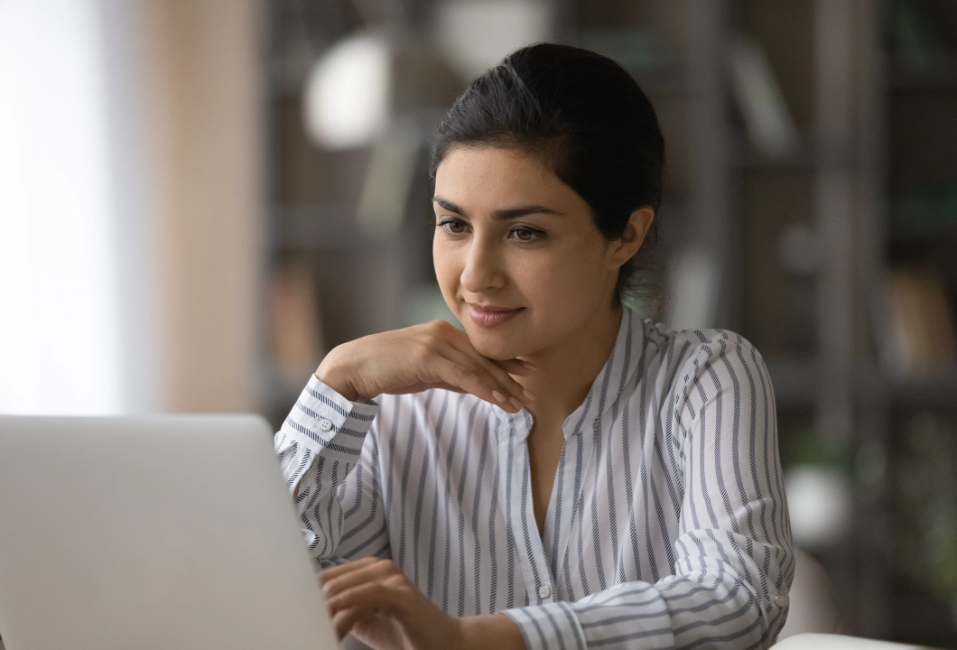 A woman in a blouse sitting in front of an open laptop computer.