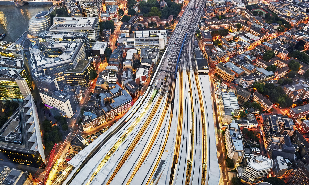 An aerial view of several trains on converging train tracks in a big city with skyscrapers.